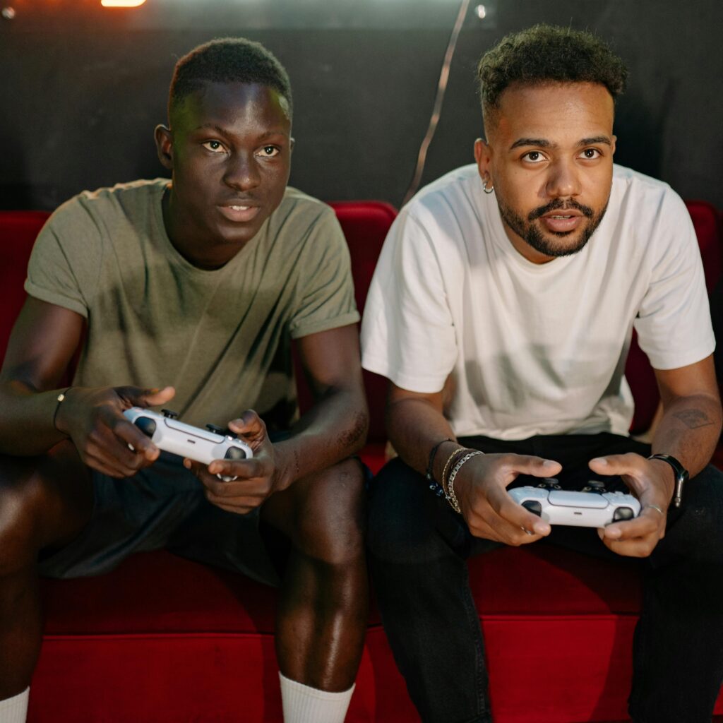 Young men playing video games on a couch with intense focus, holding controllers.
