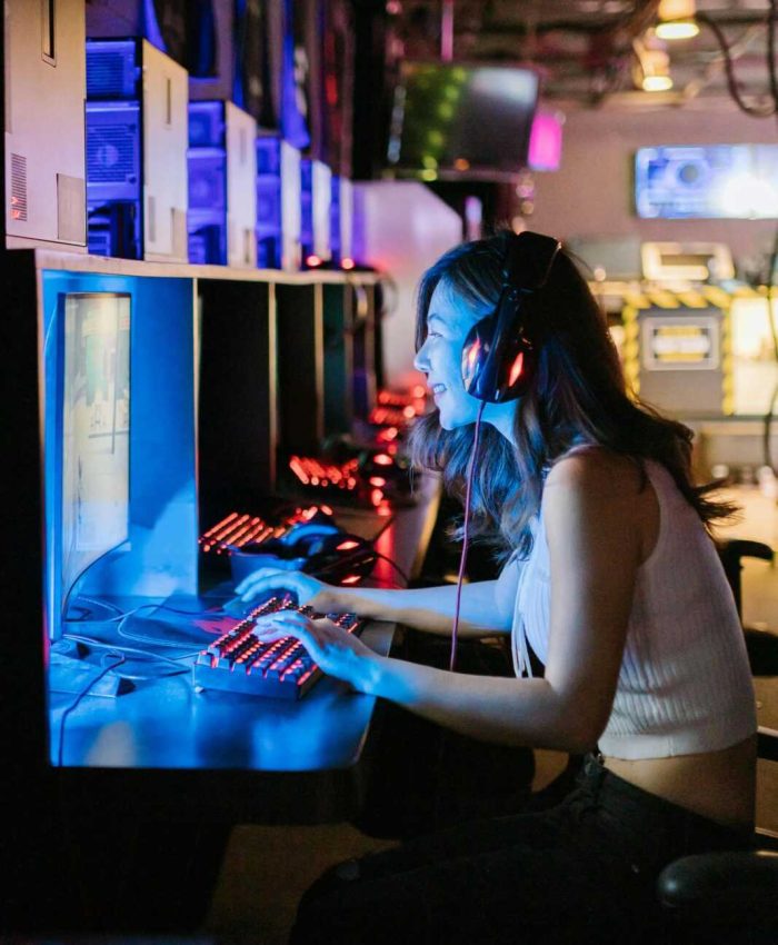 A woman intensely focused on a gaming computer in an esports setting with vibrant lighting.